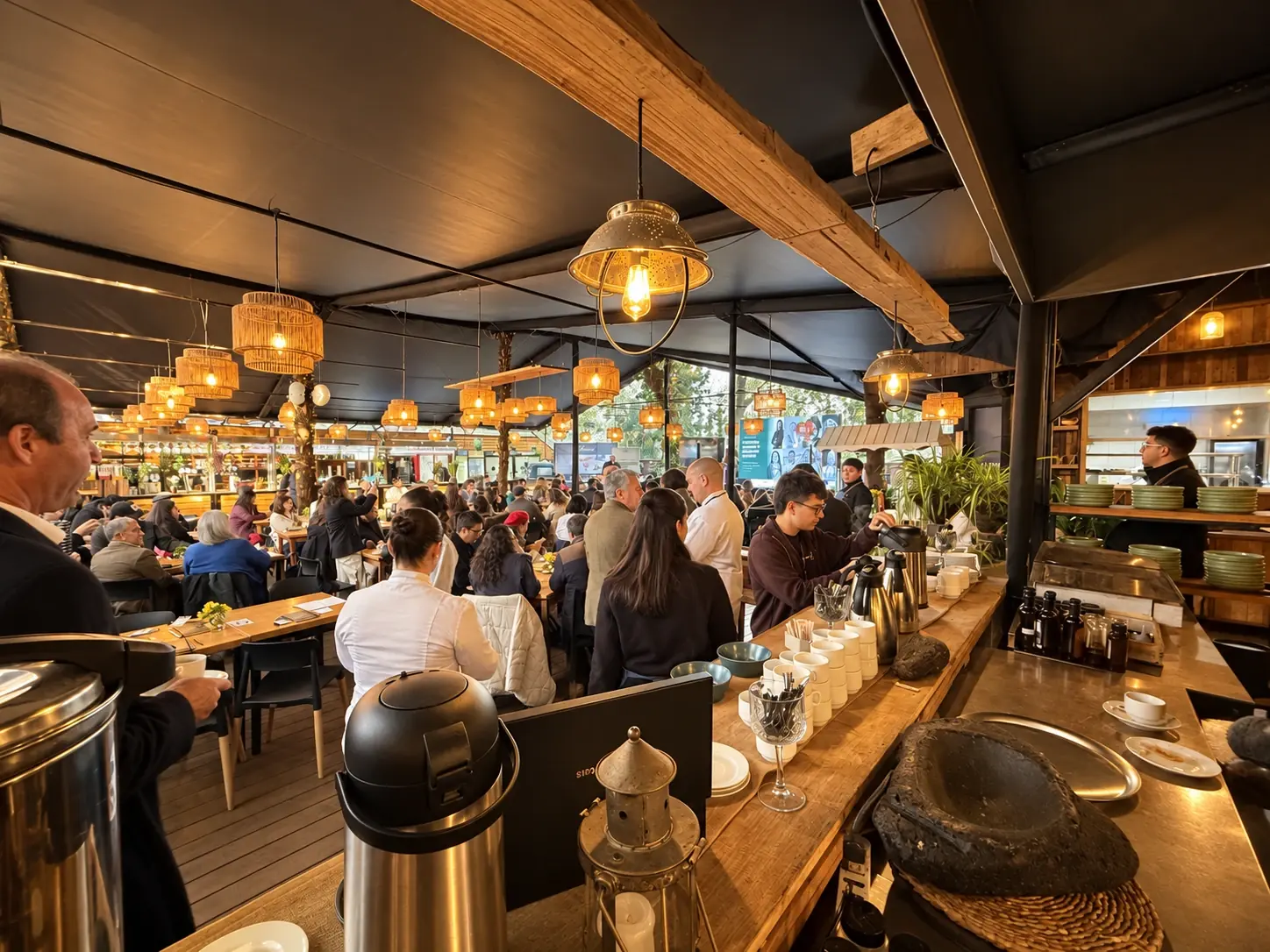 Evento corporativo en Casa Espoz: salón con techo de madera y lámparas de mimbre, mesas largas con invitados conversando y mesón de café